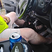Blackjack is registered to the contest to win money with this photo: cat, black_cat, person, legs, shorts, neon_shirt, car_interior, steering_wheel, dashboard, soda_can, cup_holder, hand, footwear, car_seat, vehicle, window, door, yawning_cat, sitting, casual