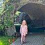 child, girl, grass, greenery, leaves, mini_golf, nature, outdoor, pathway, pink_clothing, playing, putting_green, recreation, rock_formation, sandals, smiling, summer, sunlight, trees, vine