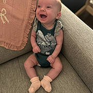 Ava joined the competition — help win amazing prizes! baby, infant, child, smiling, laughing, sitting, couch, sofa, blanket, indoors, portrait, happy, face, eyes, clothing, onesie, socks, ruffles, furniture, cozy