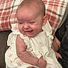 Ava joined the competition — help win amazing prizes! baby, child, infant, smiling, winking, tongue_out, portrait, sitting, couch, blanket, dress, floral_pattern, indoor, home, face, head, arms, legs, happy, family_photo