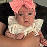 baby, infant, child, portrait, pink_bow, headband, floral_outfit, romper, wide_eyes, looking_at_camera, sitting, held, adult, arms, indoor, close_up, face, smiling, fashion, family
