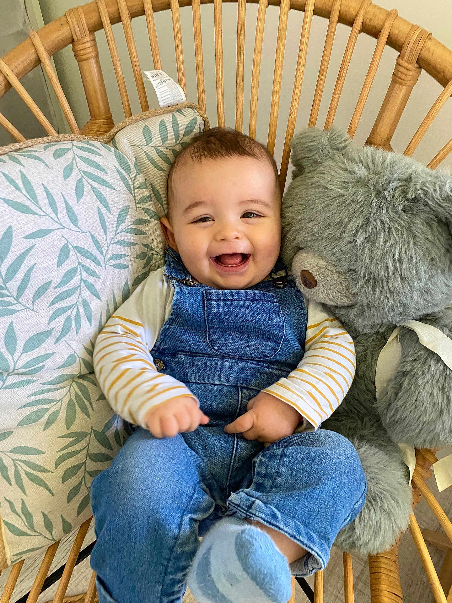 Andréas a rejoint le concours — aidez-le/la à gagner de superbes lots ! baby, child, smiling, denim_overalls, striped_shirt, sock, teddy_bear, stuffed_animal, wicker_chair, cushion, indoor, happy, cute, infant, person, portrait, seated, cozy, comfortable, playful