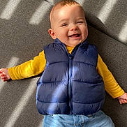 Andréas participe au concours pour gagner de l'argent avec cette photo : baby, blue_jeans, casual_clothing, child, couch, cute, face, happy, home, indoor, infant, lying_down, person, portrait, puffy_vest, relaxed, shadow, smiling, sunlight, yellow_shirt