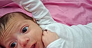 Phoenix is registered to the contest to win money with this photo: baby, infant, white_clothing, pink_blanket, bottle, lying_down, indoors, child, cute, wide_eyes, hand_up, soft_fabric, portrait, newborn, person, sleepwear, bedroom, resting, young, cozy
