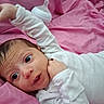 baby, infant, white_clothing, pink_blanket, bottle, lying_down, indoors, child, cute, wide_eyes, hand_up, soft_fabric, portrait, newborn, person, sleepwear, bedroom, resting, young, cozy