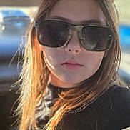 Ava is registered to the contest to win money with this photo: child, sunglasses, portrait, close_up, car_interior, sunlight, hair, face, lips, nose, skin, reflection, seatbelt, black_shirt, casual, window, bokeh_background, young_person, serious_expression, natural_light