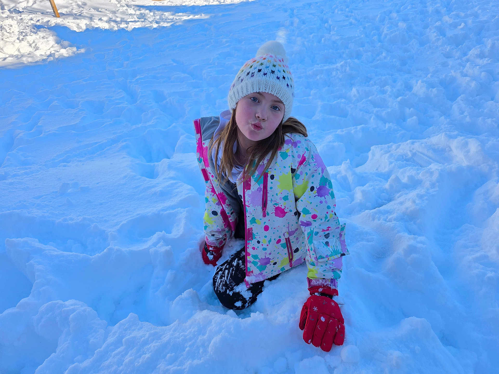 Ava joined the competition — help win amazing prizes! child, girl, snow, winter, colorful_jacket, knit_hat, beanie, red_gloves, playful, puckered_lips, smile, portrait, outdoor, cold, kneeling, snowfield, young, face, long_hair, bright_colors