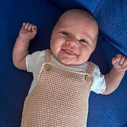 Dessa is registered to the contest to win money with this photo: baby, smiling, infant, romper, white_shirt, blue_blanket, happy, cute, portrait, child, skin, face, head, person, lying_down, hands_up, button, textile, cozy, indoors