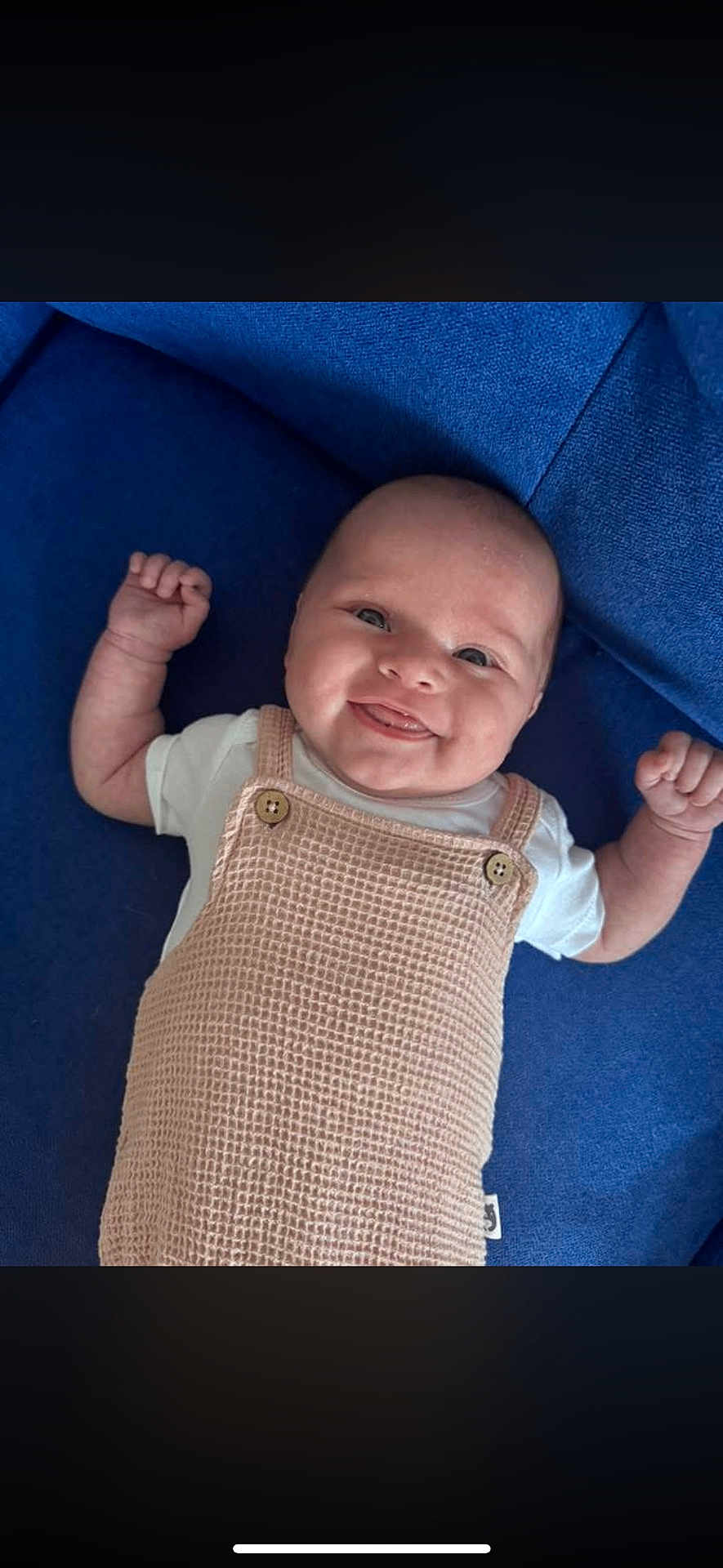 Dessa is registered to the contest to win money with this photo: baby, smiling, infant, romper, white_shirt, blue_blanket, happy, cute, portrait, child, skin, face, head, person, lying_down, hands_up, button, textile, cozy, indoors