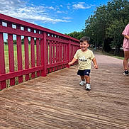 Battistu a rejoint le concours — aidez-le/la à gagner de superbes lots ! toddler, child, running, bridge, wooden_floor, red_railing, outdoor, park, trees, grass, blue_sky, clouds, adidas, shorts, tshirt, sneakers, person, happy, smiling, casual_clothing