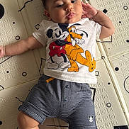 Hakim participe au concours pour gagner de l'argent avec cette photo : baby, child, mickey_mouse, pluto, tshirt, shorts, striped_clothing, patterned_mat, floor, hand, leg, foot, face, hair, curly_hair, lying_down, black_and_white, cartoon_character, indoor, person