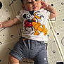 baby, child, mickey_mouse, pluto, tshirt, shorts, striped_clothing, patterned_mat, floor, hand, leg, foot, face, hair, curly_hair, lying_down, black_and_white, cartoon_character, indoor, person