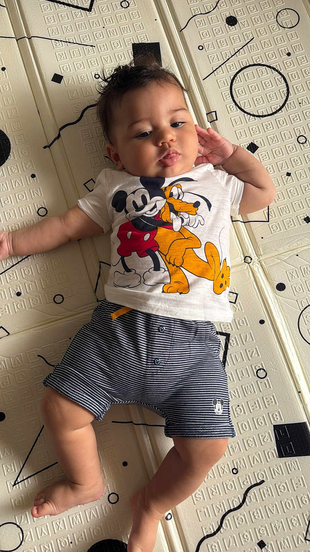Hakim participe au concours pour gagner de l'argent avec cette photo : baby, child, mickey_mouse, pluto, tshirt, shorts, striped_clothing, patterned_mat, floor, hand, leg, foot, face, hair, curly_hair, lying_down, black_and_white, cartoon_character, indoor, person