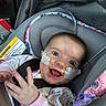 baby, infant, car_seat, smiling, medical_tube, nasal_cannula, happy, child, seat_belt, clothing, indoors, portrait, face, head_support, pink, toy, hand, eyes, healthcare, cute
