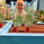 Rhett-Michael is registered to the contest to win money with this photo: child, toddler, smiling, indoor, play_area, wooden_toy, carrot_cutout, game, colorful, decor, furniture, person, face, happy, play, cute, light, wood, toy, background