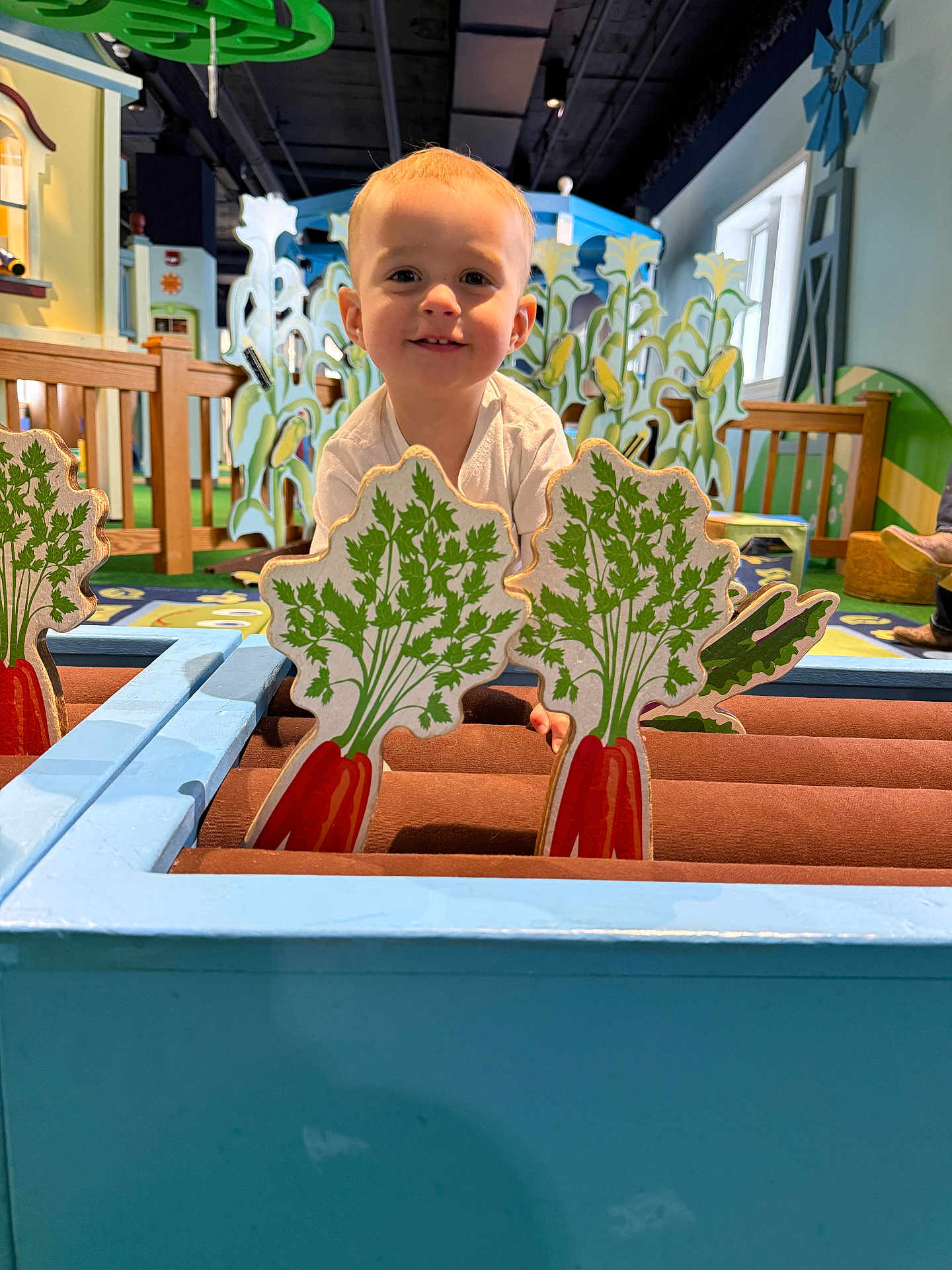 Rhett-Michael is registered to the contest to win money with this photo: child, toddler, smiling, indoor, play_area, wooden_toy, carrot_cutout, game, colorful, decor, furniture, person, face, happy, play, cute, light, wood, toy, background