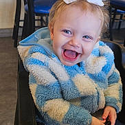 Aryah is registered to the contest to win money with this photo: toddler, child, smiling, high_chair, bow, jacket, blue, white, indoor, restaurant, table, chair, happy, person, cute, laughing, baby, hair, clothing, seat