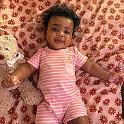 Kameryn is registered to the contest to win money with this photo: baby, infant, smiling, curly_hair, pink_clothing, striped_outfit, teddy_bear, stuffed_animal, blanket, floral_pattern, lying_down, cute, child, indoors, happy, portrait, soft_toys, baby_girl, pajamas, playful