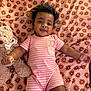baby, infant, smiling, curly_hair, pink_clothing, striped_outfit, teddy_bear, stuffed_animal, blanket, floral_pattern, lying_down, cute, child, indoors, happy, portrait, soft_toys, baby_girl, pajamas, playful