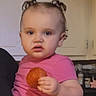 Bailey is registered to the contest to win money with this photo: toddler, child, curly_hair, pink_shirt, snack, kitchen, indoor, person, face, hand, food, young_child, casual_clothing, expression, portrait, holding, cute, baby, young, domestic