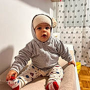Mattéo participe au concours pour gagner de l'argent avec cette photo : baby, child, hoodie, hat, socks, indoor, curtain, soccer_ball_pattern, floor, wooden_floor, blanket, seated, portrait, cute, warm_clothing, person, furniture, curious, soft_surface, home