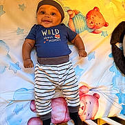 Idris joined the competition — help win amazing prizes! baby, child, infant, smiling, happy, portrait, crib, blanket, star_pattern, teddy_bear, striped_clothing, hat, blue_shirt, black_socks, lying_down, indoor, nursery, bedroom, colorful, photography