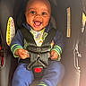 baby, child, infant, smiling, happy, portrait, car_seat, safety_harness, buckled, automobile, seated, indoor, close_up, face, eyes, open_mouth, colorful_clothing, blue_pants, green_stripes, photography