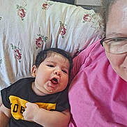 Danny joined the competition — help win amazing prizes! baby, infant, person, couch, pillow, floral_pattern, black_shirt, yellow_text, glasses, pink_shirt, smile, face, indoor, curly_hair, expression, hand, cozy, family, cute, relaxed