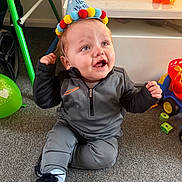 Hunter is registered to the contest to win money with this photo: baby, child, birthday_hat, sitting, carpet, toy, balloon, smiling, clothing, shoe, sock, indoor, happy, face, person, playtime, celebration, floor, colorful, young_child