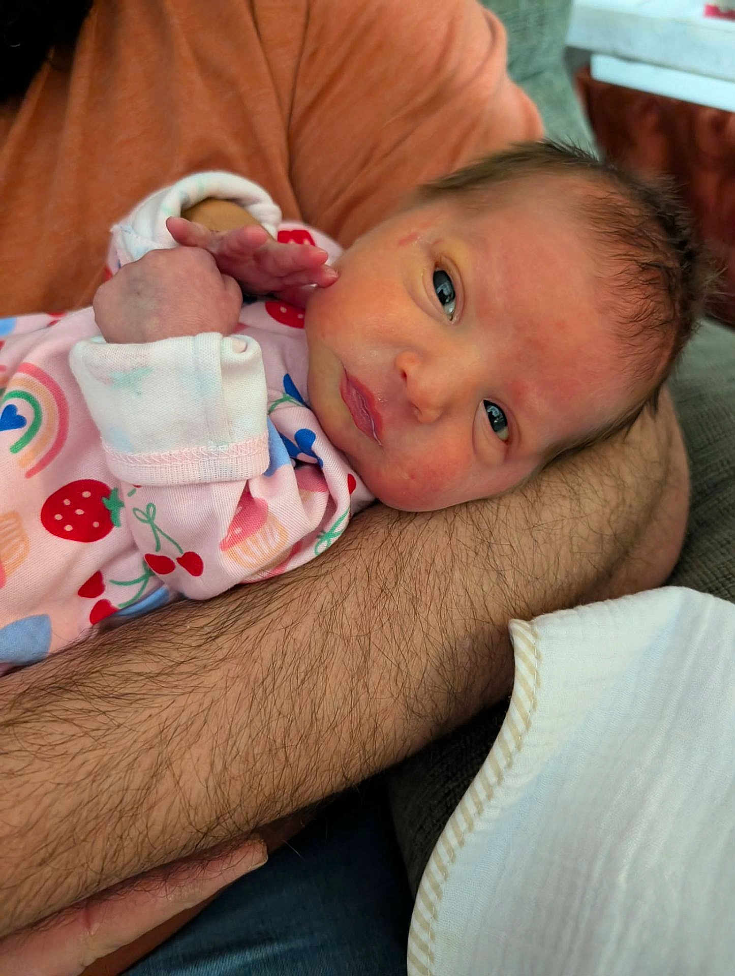 Evangeline joined the competition — help win amazing prizes! baby, newborn, infant, arm, person, clothing, onesie, patterned_clothing, fruit_pattern, rainbow_pattern, indoor, couch, blanket, resting, face, skin, hair, hand, closeup, comfort