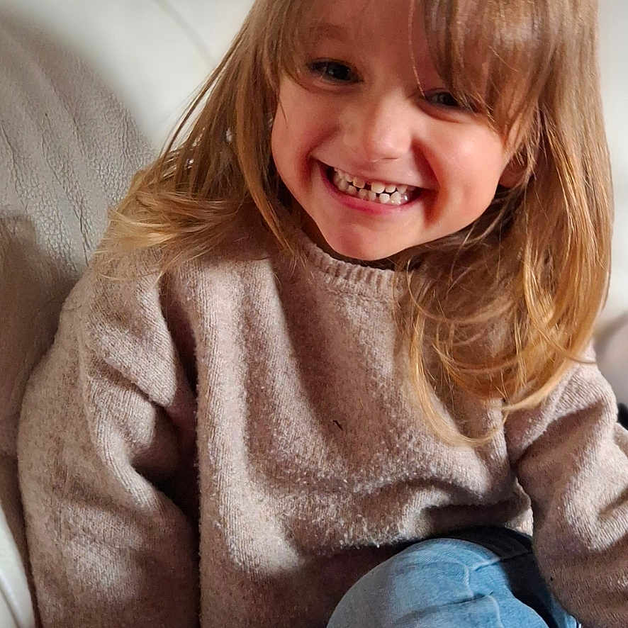 Lyvianah participe au concours pour gagner de l'argent avec cette photo : child, smiling, happy, sitting, couch, sweater, blue_jeans, long_hair, indoors, portrait, young_child, cozy, casual_clothing, cute, face, person, home, relaxed, joyful, natural_light