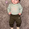 Alena is registered to the contest to win money with this photo: baby, child, infant, carpet, clothing, pacifier, green_clothes, bow_design, footwear, lying_down, portrait, indoors, cute, curious, soft_texture, headband, expression, small_hands, casual_wear, baby_shoes