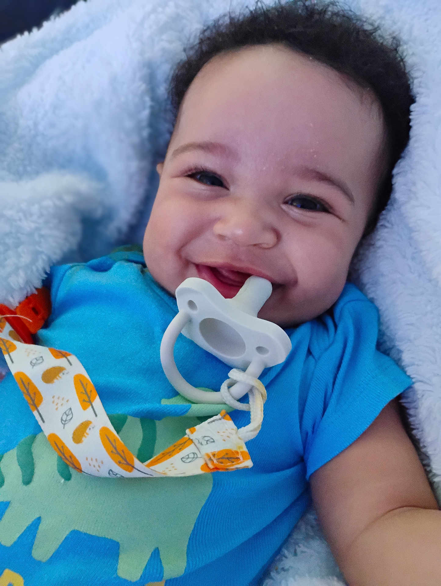 Marcus joined the competition — help win amazing prizes! baby, smiling, pacifier, blue_shirt, dinosaur_print, blanket, infant, happy, face, cute, child, clothing, closeup, lying_down, skin, person, indoors, comfort, baby_accessory, portrait