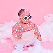 Eline a rejoint le concours — aidez-le/la à gagner de superbes lots ! baby, child, pink_background, sunglasses, headband, flower_glasses, tulle_skirt, patterned_sweater, white_tights, sitting, fluffy_clouds, studio_photo, cute, fashion, portrait, indoor, adorable, smiling, infant, soft_texture