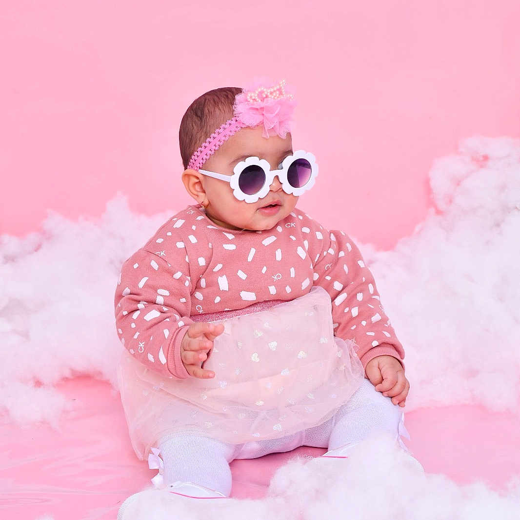 Eline a rejoint le concours — aidez-le/la à gagner de superbes lots ! adorable, baby, child, cute, fashion, flower_glasses, fluffy_clouds, headband, indoor, infant, patterned_sweater, pink_background, portrait, sitting, smiling, soft_texture, studio_photo, sunglasses, tulle_skirt, white_tights