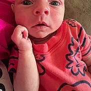 Holden joined the competition — help win amazing prizes! baby, infant, child, close_up, face, hand, orange_shirt, patterned_clothing, couch, indoor, living_room, bookshelf, dvd, curious, resting, wide_eyes, soft_furniture, portrait, young_child, casual_clothing