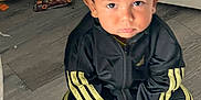 Huxley is registered to the contest to win money with this photo: barefoot, black_clothing, boy, cap, casual, child, clothing, floor, flooring, home, indoor, laundry_basket, person, serious_expression, shoes, sitting, tracksuit, wooden_floor, yellow_stripes, young_child