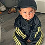 Huxley is registered to the contest to win money with this photo: child, boy, cap, tracksuit, black_clothing, yellow_stripes, barefoot, floor, wooden_floor, laundry_basket, shoes, indoor, serious_expression, sitting, casual, home, clothing, person, young_child, flooring
