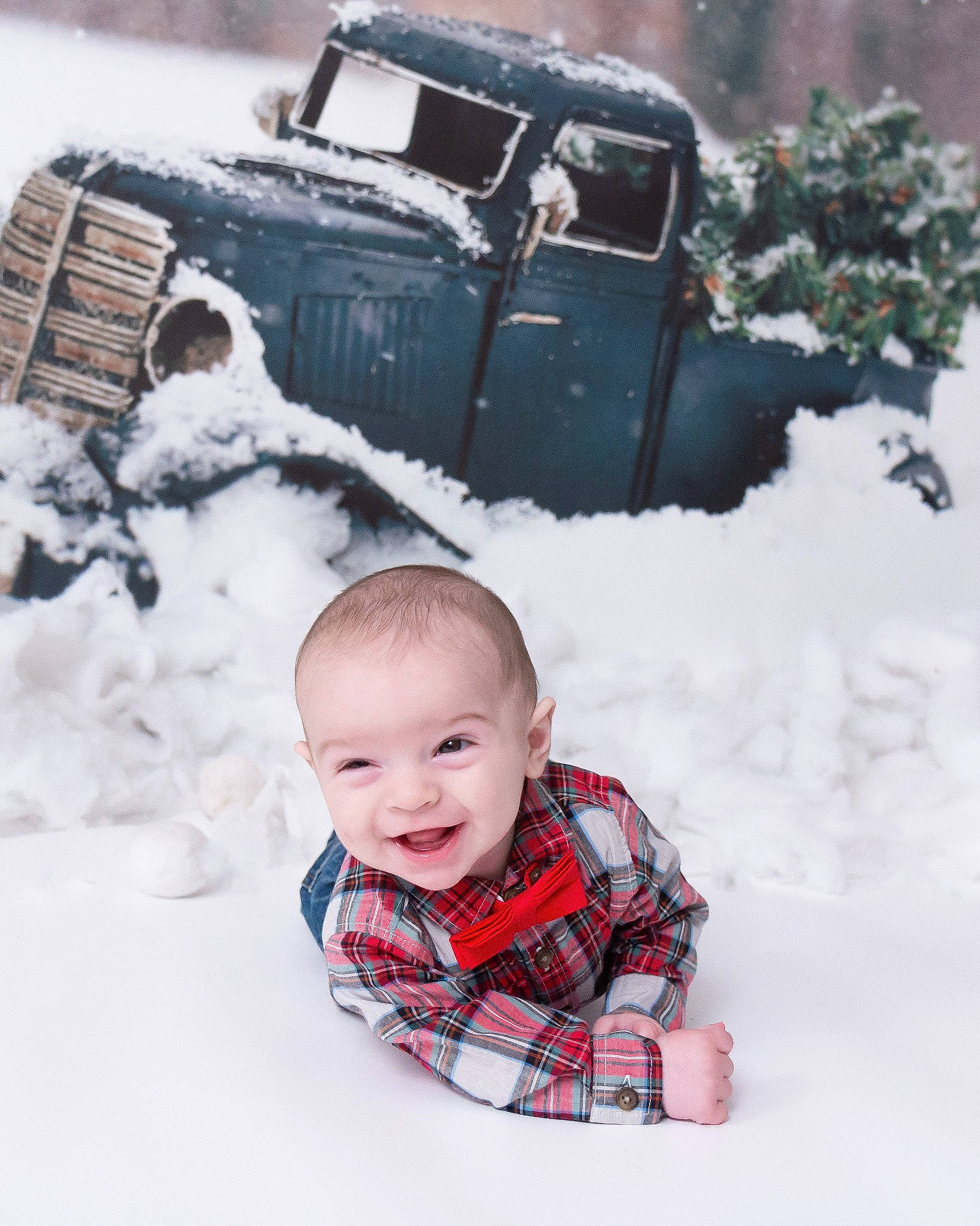Levi is registered to the contest to win money with this photo: automotive_tire, baby, baby_toddler_clothing, collar, face, freezing, human_body, jacket, joy, pattern, person, photograph, plaid, sleeve, smile, snapshot, snow, tartan, toddler, tree
