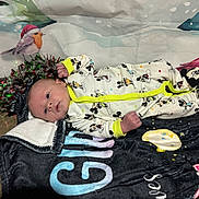 Wyatt is registered to the contest to win money with this photo: baby, infant, mickey_mouse, onesie, blanket, holiday_decor, tinsel, bird_illustration, floor, face, person, cute, lying_down, indoor, colorful, festive, soft_texture, child, newborn, footwear