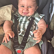 Jack is registered to the contest to win money with this photo: baby, child, car_seat, seatbelt, smiling, green_clothing, striped_shirt, plush_toy, blanket, chubby_arms, chubby_legs, face, happy, infant, seated, indoors, cute, person, closeup, safety