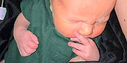 Christopher joined the competition — help win amazing prizes! baby, infant, newborn, clothing, green_onesie, blanket, black_blanket, white_blanket, hand, face, skin, head, hair, sleepy, cute, person, baby_fashion, indoors, closeup, wrapping