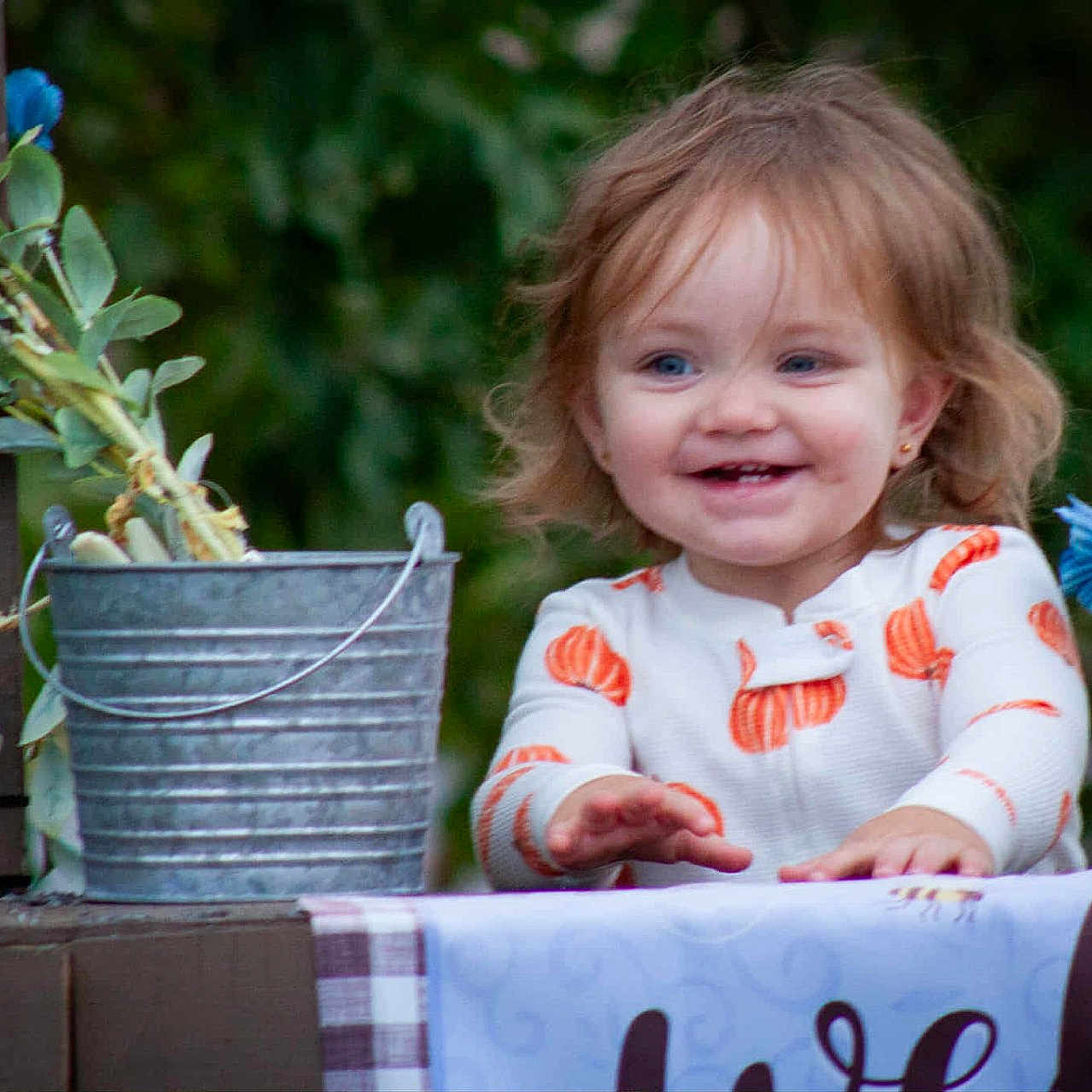 Amari joined the competition — help win amazing prizes! baby, blue_eyes, child, clothing, decor, face, flowers, greenery, happy, light_hair, long_sleeve, metal_bucket, outdoor, person, smiling, table, tablecloth, toddler, welcome_sign, wood