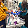 Weston is registered to the contest to win money with this photo: newborn, baby, hospital, medical_staff, gloves, hospital_bassinet, monitor, medical_equipment, person, healthcare, care, infant, patient, scrubs, yellow_hoodie, bed, blanket, foot, hand, clinic