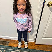 Arya is registered to the contest to win money with this photo: child, clothing, curlyhair, door, face, female, footwear, girl, hair, head, knitwear, mat, pants, person, photography, portrait, shoe, standing, sweater, wood