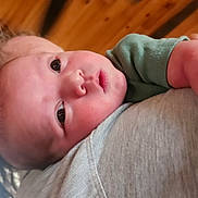 Zaiden is registered to the contest to win money with this photo: baby, infant, child, person, face, head, skin, clothing, green_shirt, grey_shirt, shoulder, indoors, wood_ceiling, curious, closeup, portrait, human, young, resting, holding