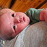 baby, infant, child, person, face, head, skin, clothing, green_shirt, grey_shirt, shoulder, indoors, wood_ceiling, curious, closeup, portrait, human, young, resting, holding
