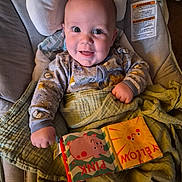 Michael is registered to the contest to win money with this photo: baby, infant, smiling, portrait, onesie, patterned_clothing, blanket, car_seat, cushion, cloth_book, baby_book, pink, yellow, hand, eyes, mouth, indoors, cheerful, close_up, warning_label