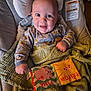 baby, infant, smiling, portrait, onesie, patterned_clothing, blanket, car_seat, cushion, cloth_book, baby_book, pink, yellow, hand, eyes, mouth, indoors, cheerful, close_up, warning_label