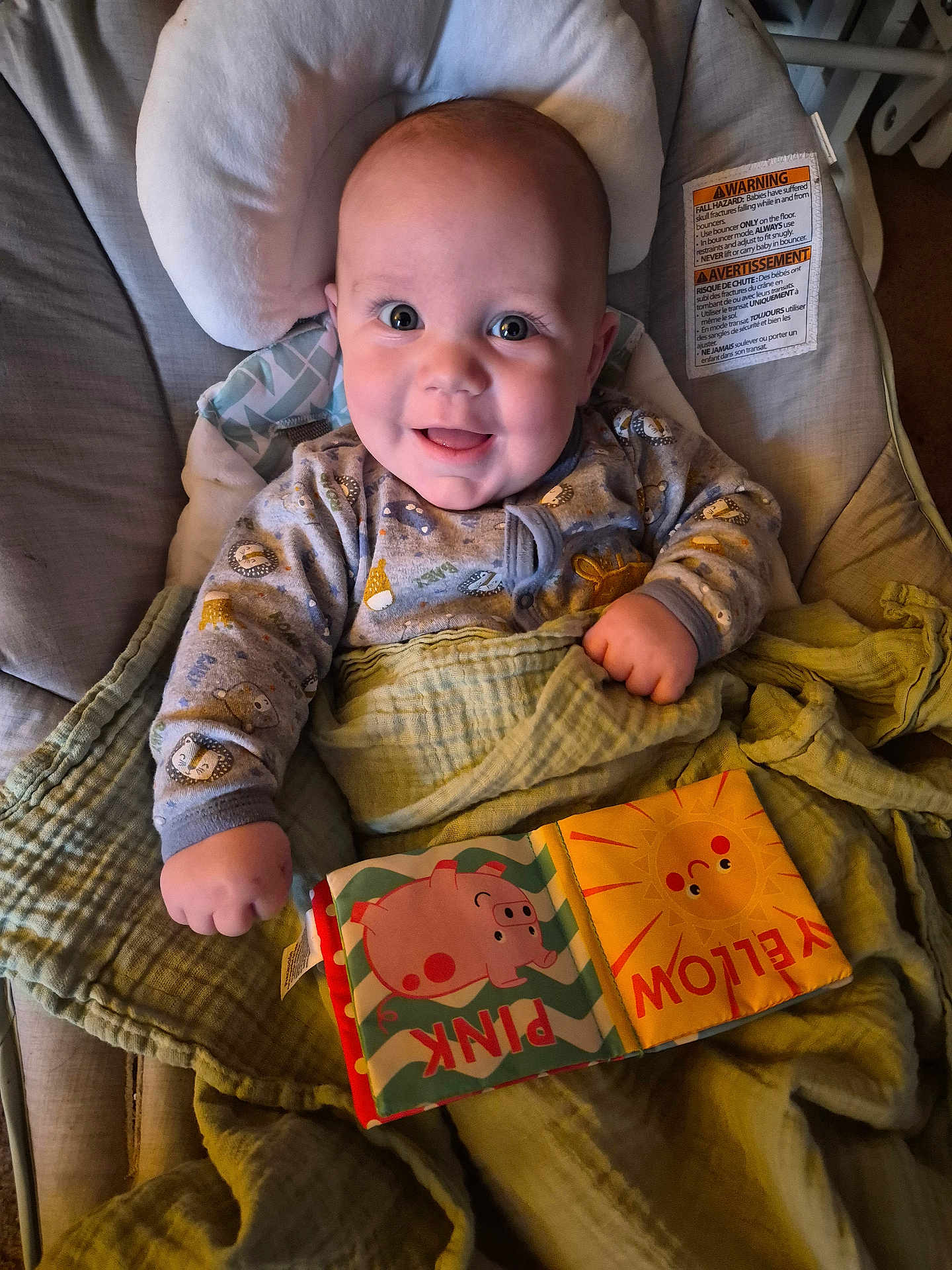 Michael is registered to the contest to win money with this photo: baby, infant, smiling, portrait, onesie, patterned_clothing, blanket, car_seat, cushion, cloth_book, baby_book, pink, yellow, hand, eyes, mouth, indoors, cheerful, close_up, warning_label